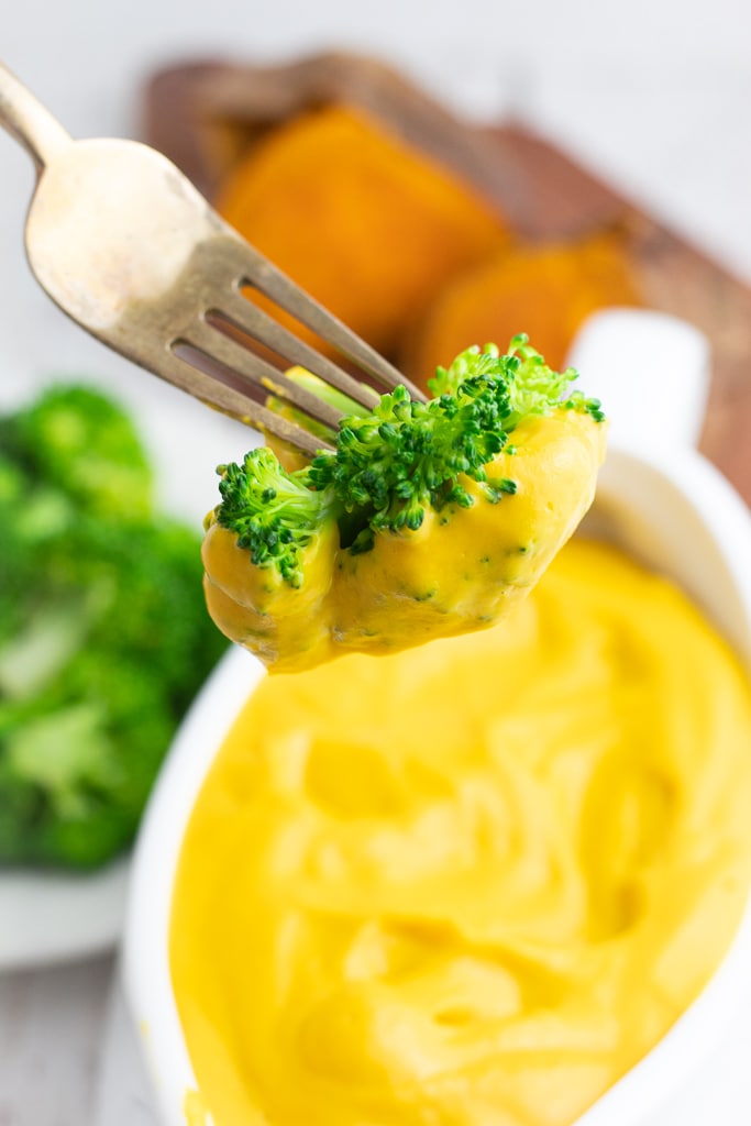 close up of fork holding a piece of broccoli covered with vegan cheese sauce