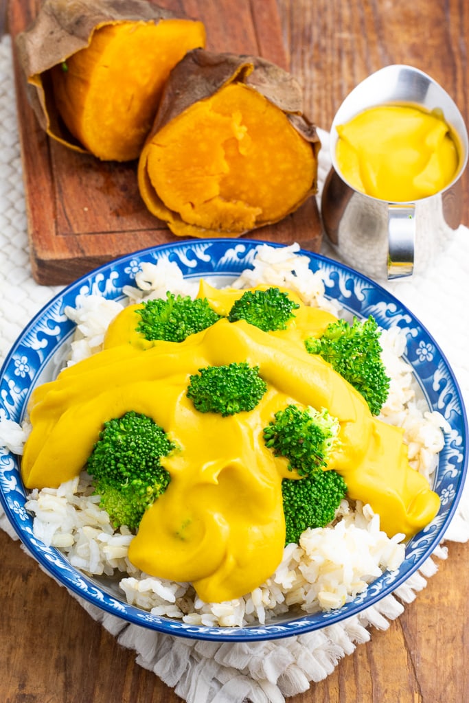 bright blue and white bowl of rice topped with broccoli and vegan cheese sauce on wooden tabletop