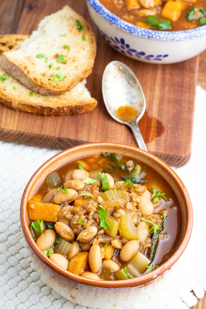 brown bowl of white bean chili with crusty bread in background