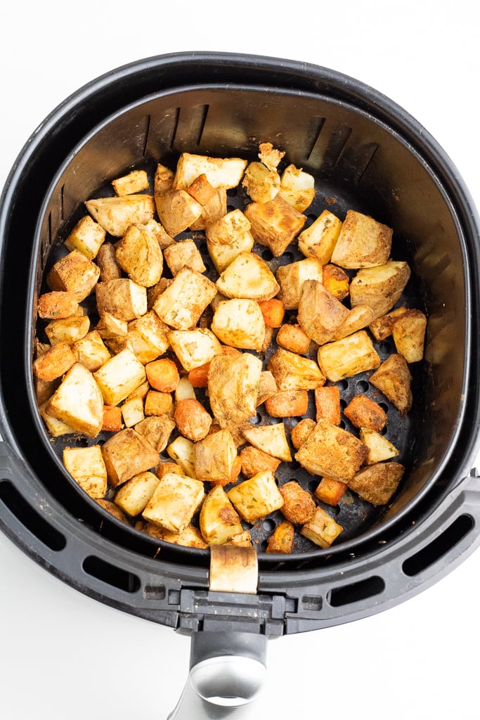 black air fryer filled with seasoned potatoes and carrots