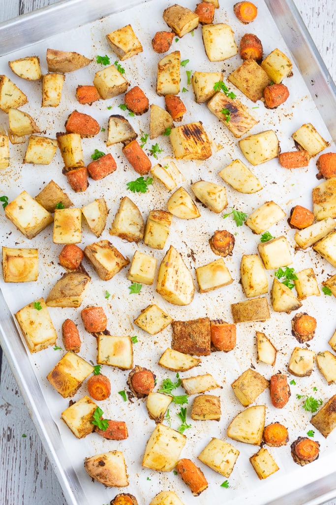 baking sheet lined with parchment paper and baked diced and seasoned potatoes and carrots