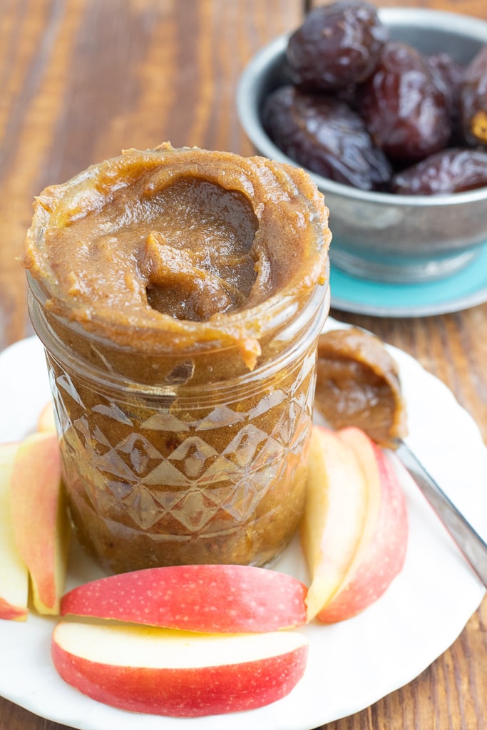 small mason jar filled with vegan date caramel with dates in background