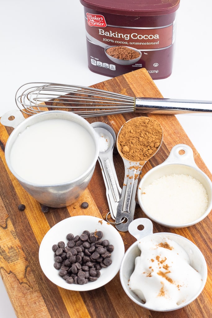 ingredients for vegan hot chocolate on wooden cutting board with cocoa and whisk