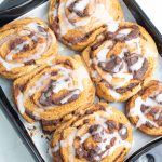 black baking pan with 6 cinnamon rolls with icing