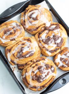 black baking pan with 6 cinnamon rolls with icing