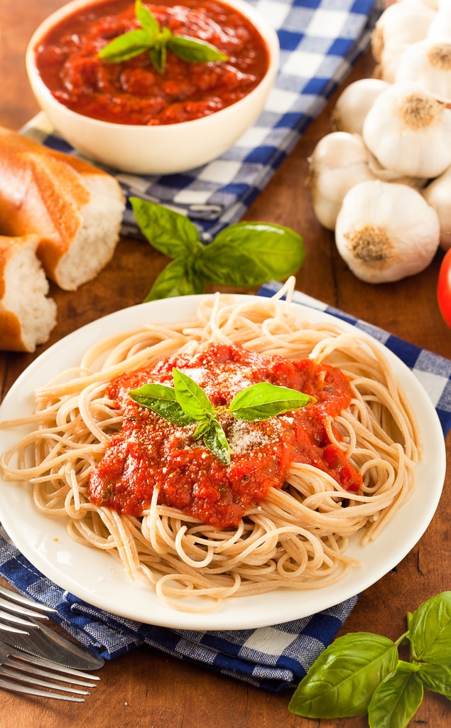 white plate filled with spaghetti pasta and fresh tomato marinara sauce topped with basil leaves
