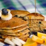 stack of cornmeal pancakes with maple syrup being poured