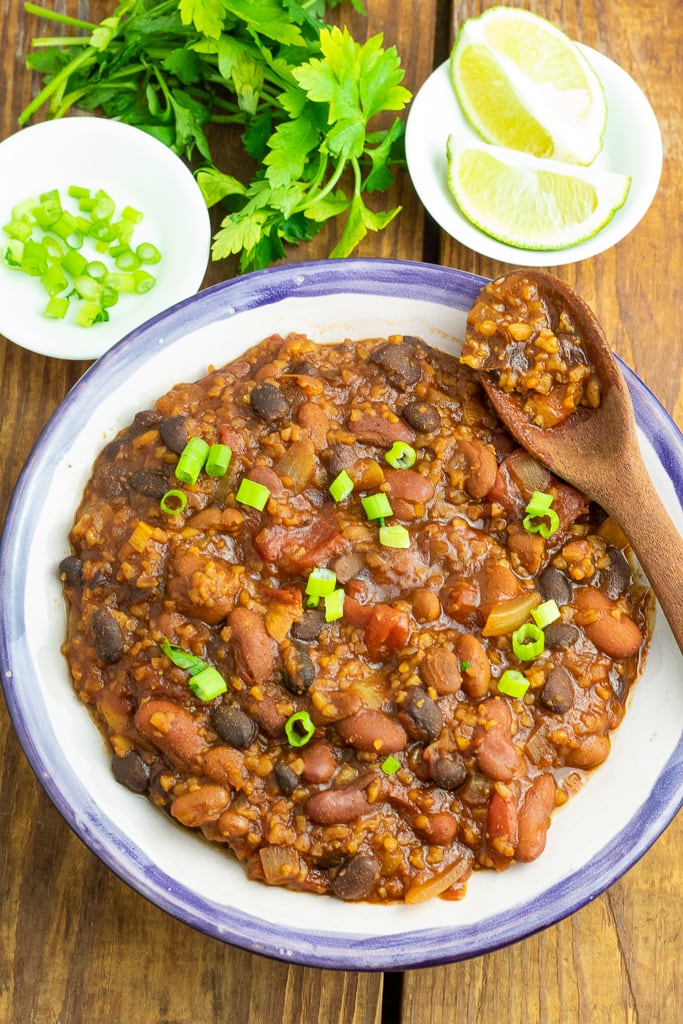 bowl of vegan chili on wooden table with wood spoon