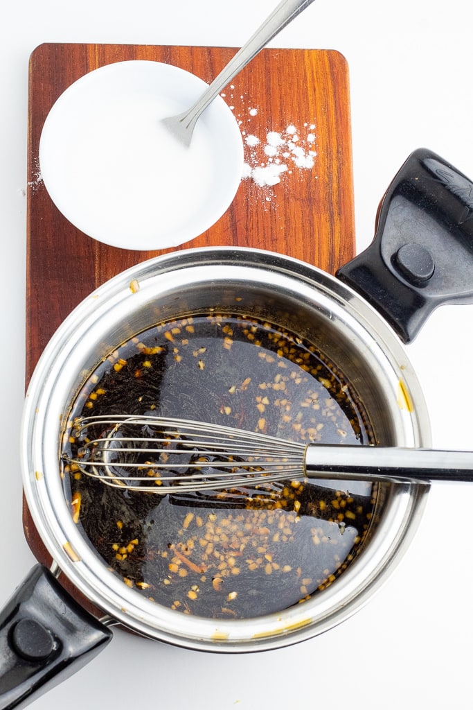 stainless saucepan with teriyaki sauce and whisk and bowl of thickener