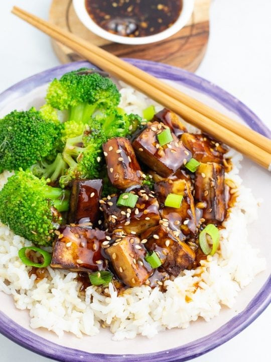 bowl filled with rice and tofu teriyaki with broccoli and chopsticks