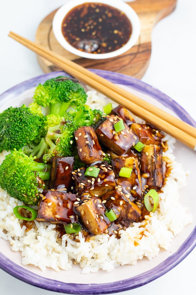 bowl filled with rice and tofu teriyaki with broccoli and chopsticks