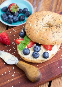 healthy bagel with vegan cream cheese and berries on cutting board