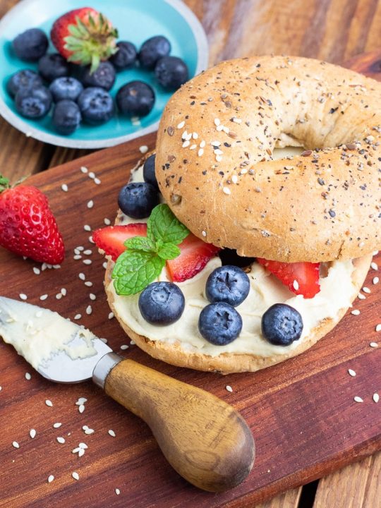 healthy bagel with vegan cream cheese and berries on cutting board