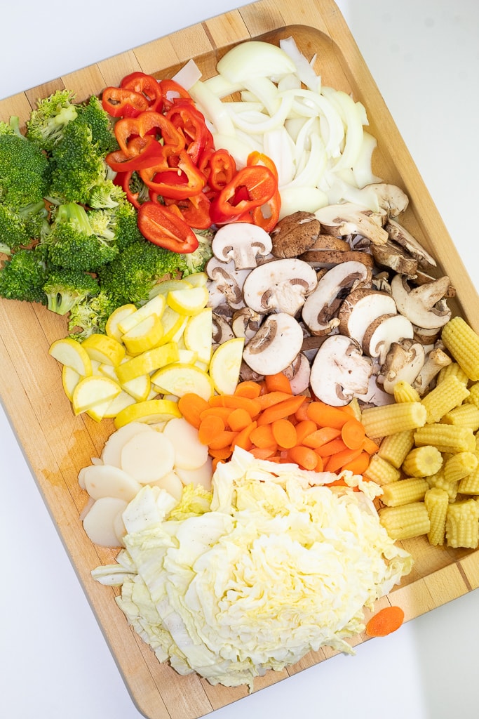 wood cutting board with broccoli, onions, carrots, mushrooms, and ba