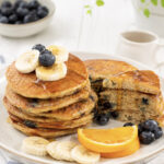 plate of cornmeal pancakes topped with blueberries and maple syrup.