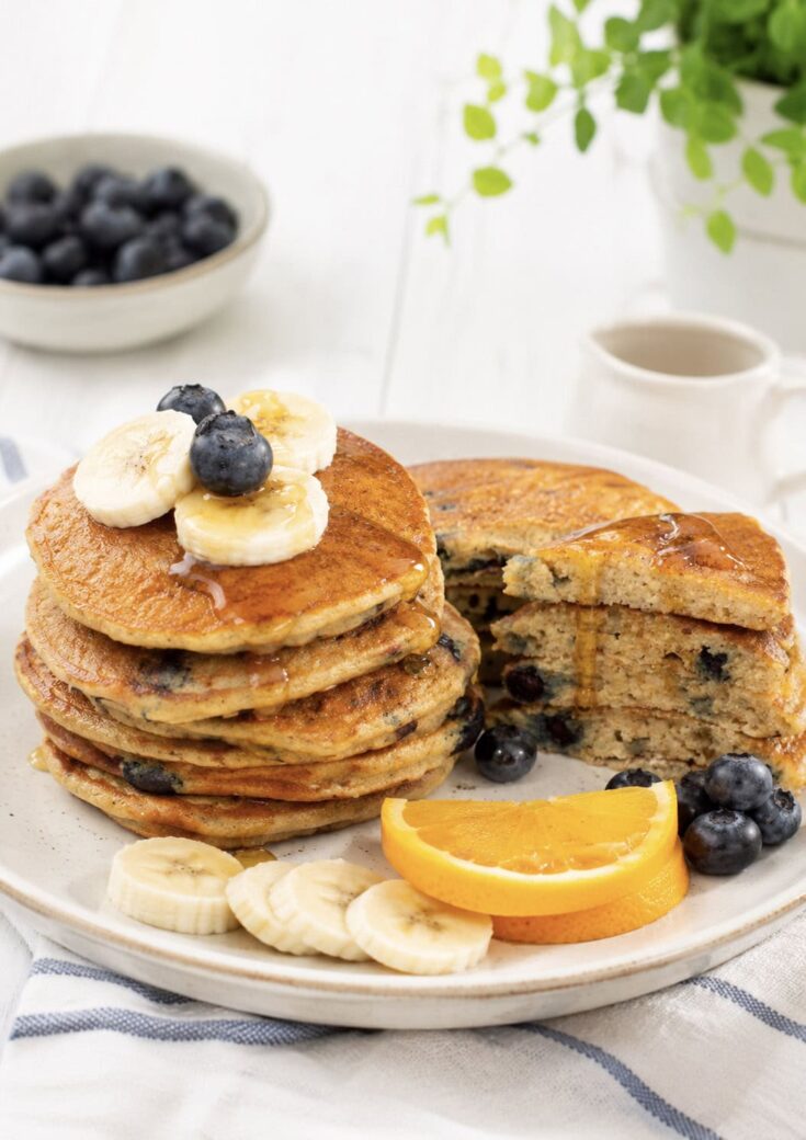 plate of cornmeal pancakes topped with blueberries and maple syrup.