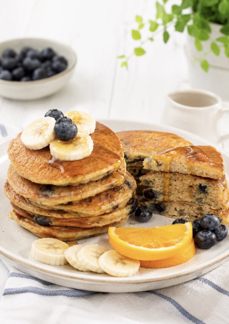 plate of cornmeal pancakes topped with blueberries and maple syrup.