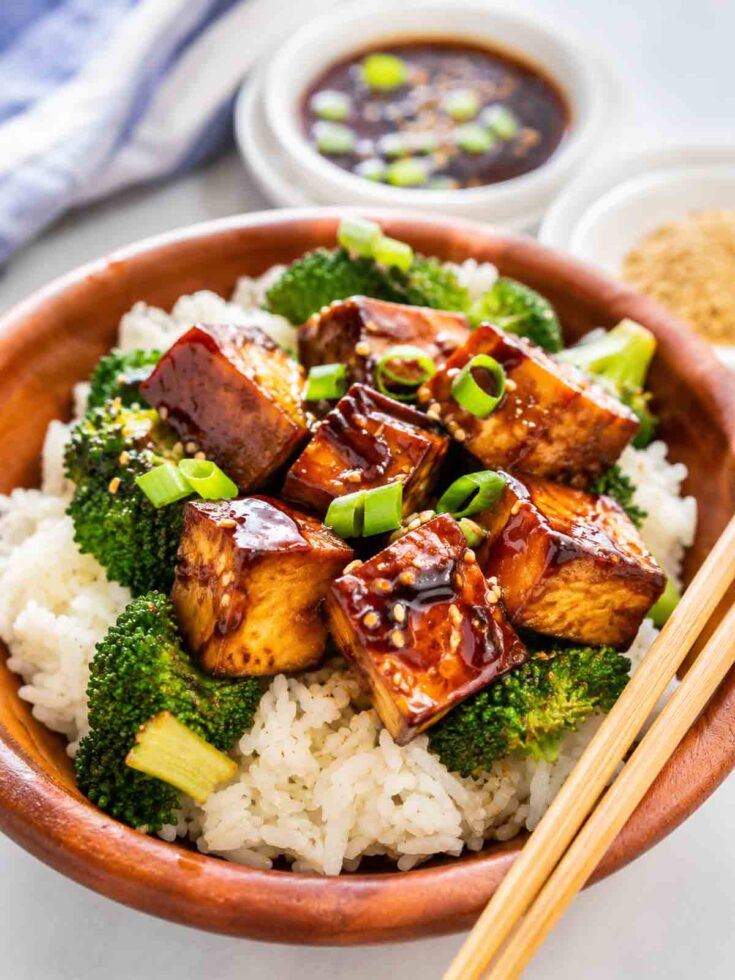 wooden bowl of brown rice topped with tofu teriyaki and broccoli.