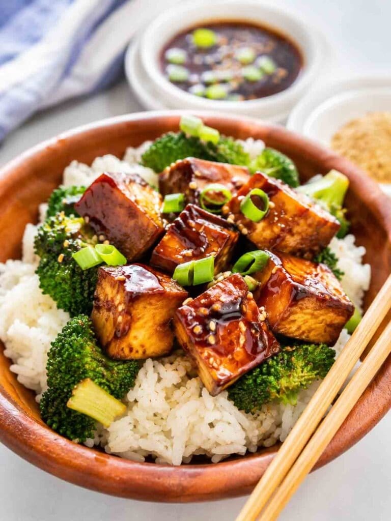 wooden bowl of brown rice topped with tofu teriyaki and broccoli.