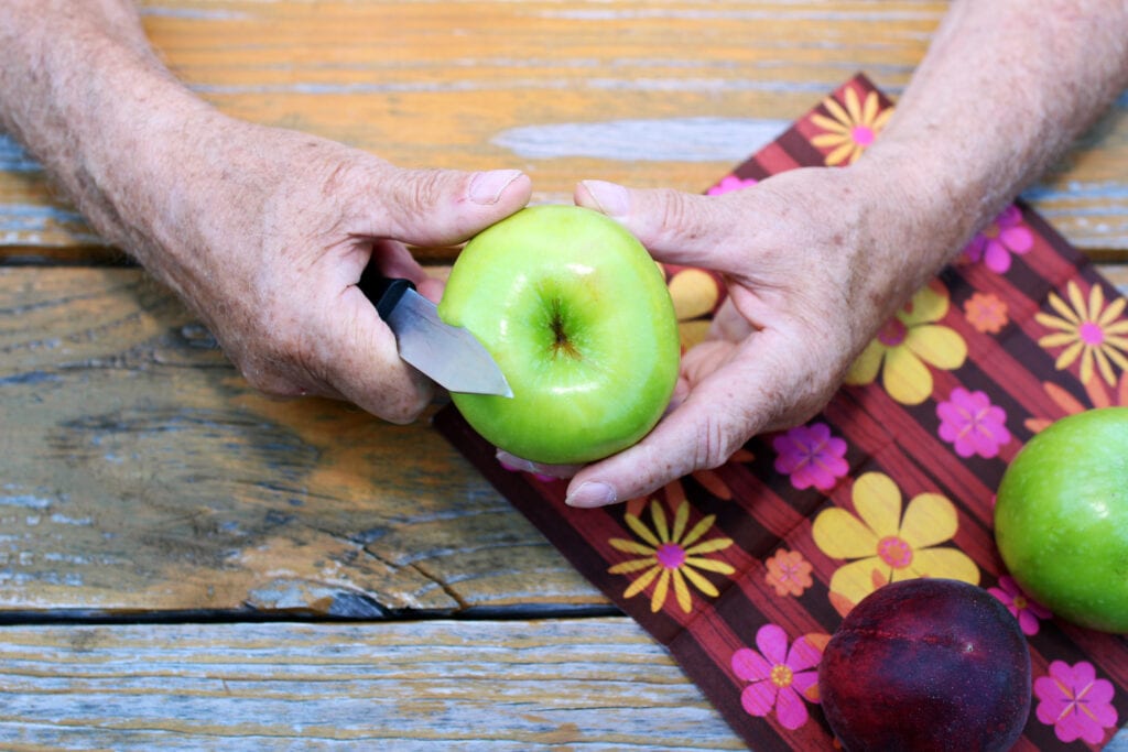 A close up of elderly man's hands peeling an apple