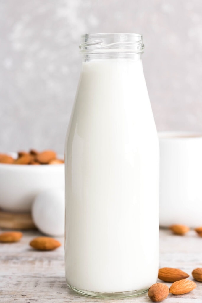 almond milk in bottle with almonds on tabletop and light background