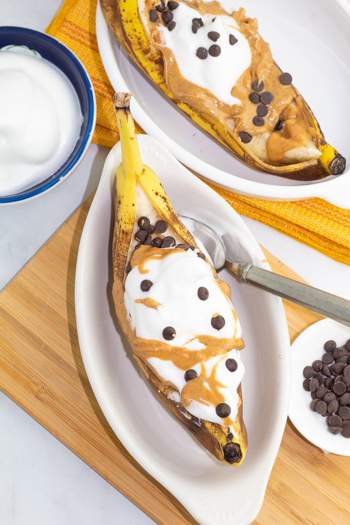 white oval dishes with banana boats topped with vegan whipped cream and chocolate chips