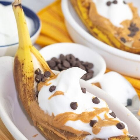 close up of banana boat dessert in white dish topped with chocoloate and peanut butter