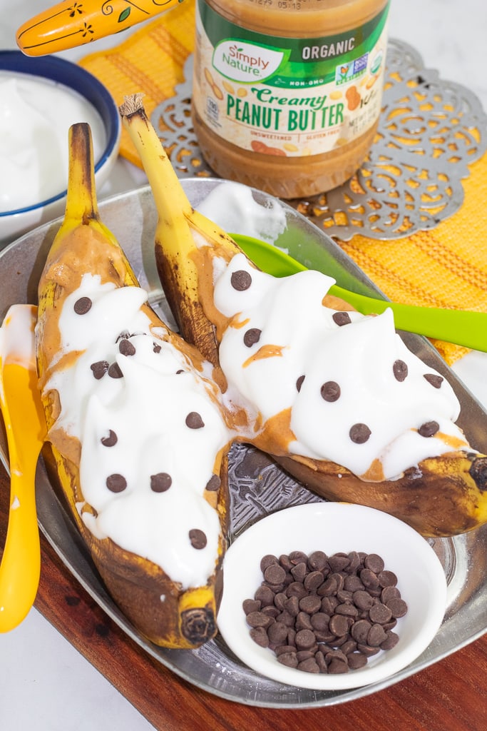 two stuffed banana boats in silver tray with white dish full of chocolate chips