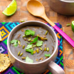 overhead shot of black bean soup in brown soup mug on colorful napkin with wooden spoon
