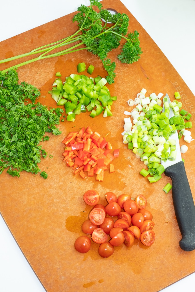 green onion, cherry tomatoes, red bell pepper, celery, and parsley chopped on cutting board with knife