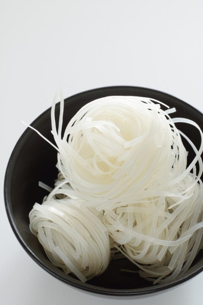 black bowl with uncooked pad thai rice noodles on white background