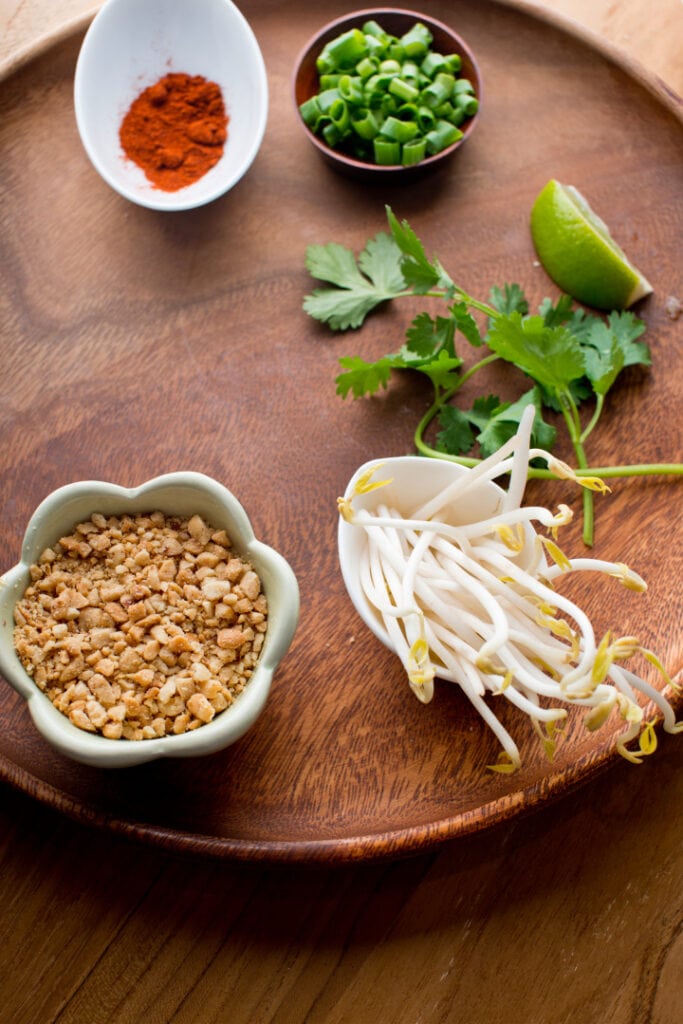 wooden dish with pad thai toppings of bean sprouts, peanuts, green onions, cilantro