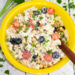 bright yellow bowl with vegan pasta salad with wooden spoon