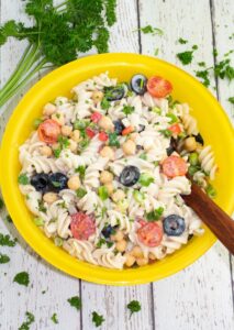 bright yellow bowl with vegan pasta salad with wooden spoon