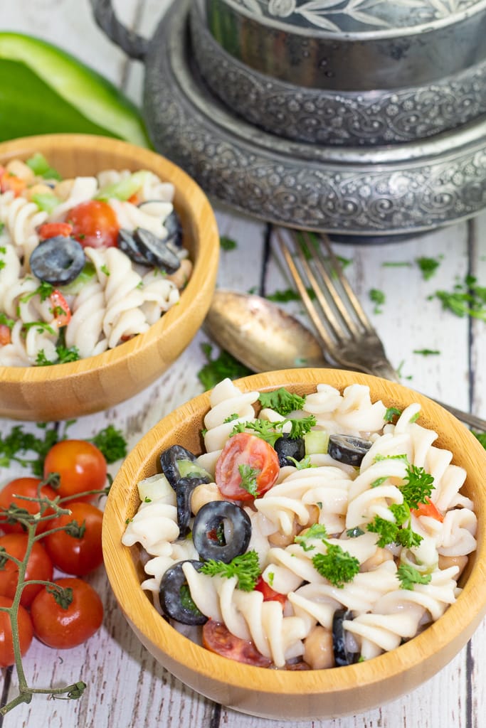 two wooden bowls filled with pasta salad on white farm board background
