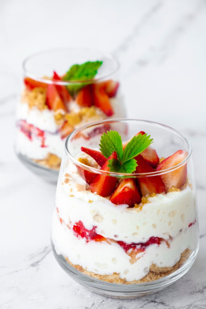 2 glasses filled with vegan yogurt topped with strawberries and granola with mint leaf