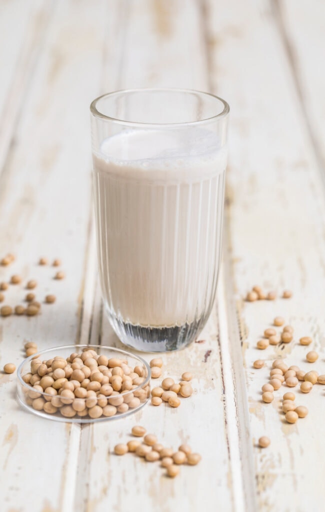 soy milk in glass with soy beans on table beside it