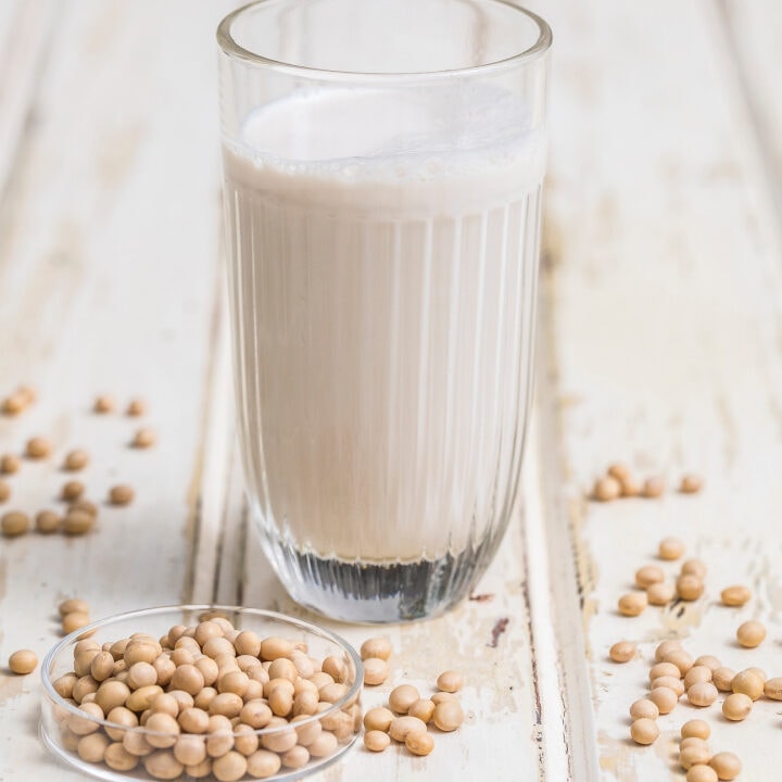 soy milk in glass with soy beans on table beside it