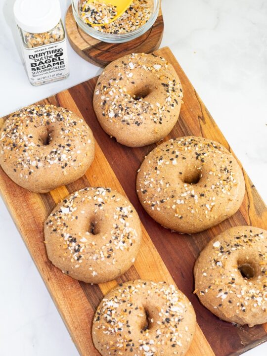 overhead shot of whole wheat bagels on wooden cutting board and sprinkled with everything but the bagel seasoning