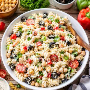pasta salad with chickpeas, black olives, tomatoes, bell peppers, parsley, and creamy dressing.