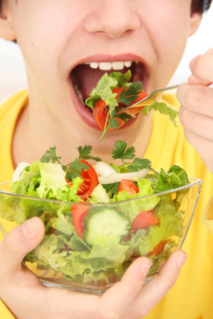 close up of young boy eating a bowl of salad