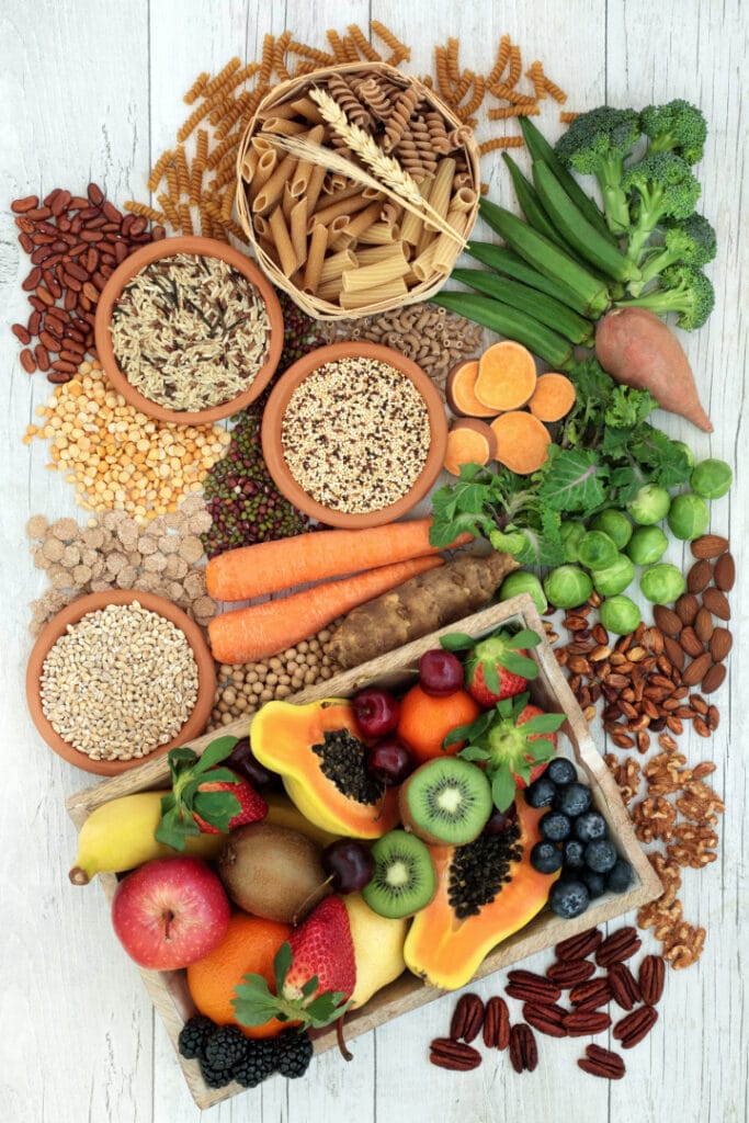 Health food for a high fiber diet with whole wheat pasta, grains, legumes, nuts, fruit, vegetables and cereals with foods high in omega 3 fatty acids, antioxidants and vitamins. Rustic background top view.