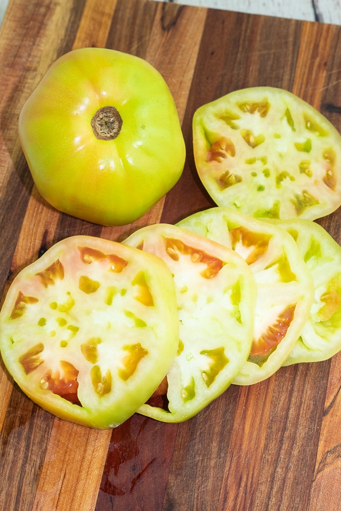slices of green tomatoes on wooden cutting board with a whole green tomato beside
