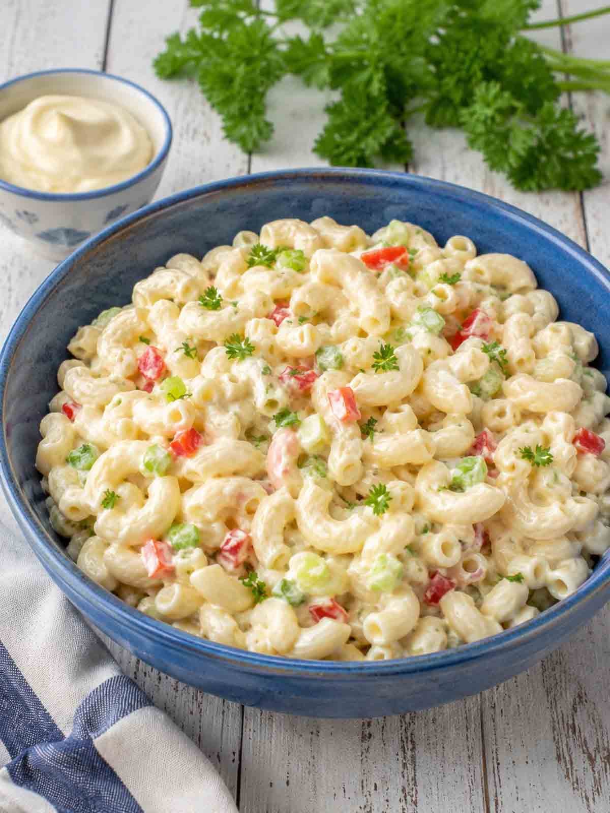 dairy-free macaroni salad in a blue bowl with vegan mayo in background.