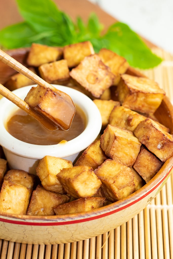chopsticks holding crispy tofu over a bowl of sweet and sour sauce