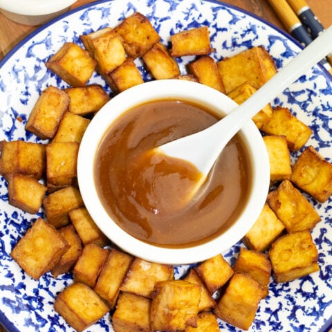 colorful blue and white plate filled with fried tofu with white bowl of sweet and sour sauce in middle with white spoon for serving