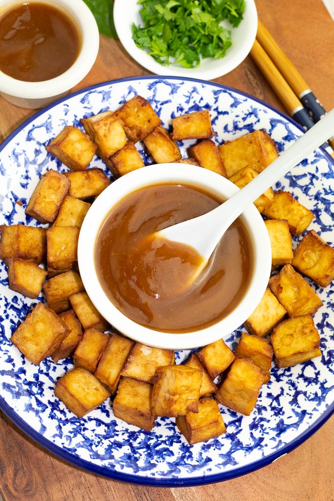 colorful blue and white plate filled with fried tofu with white bowl of sweet and sour sauce in middle with white spoon for serving