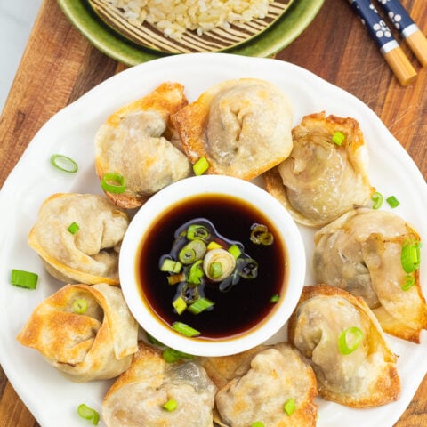 overhead photo of white plate full of vegan dumplings with dipping sauce in the middle of plate