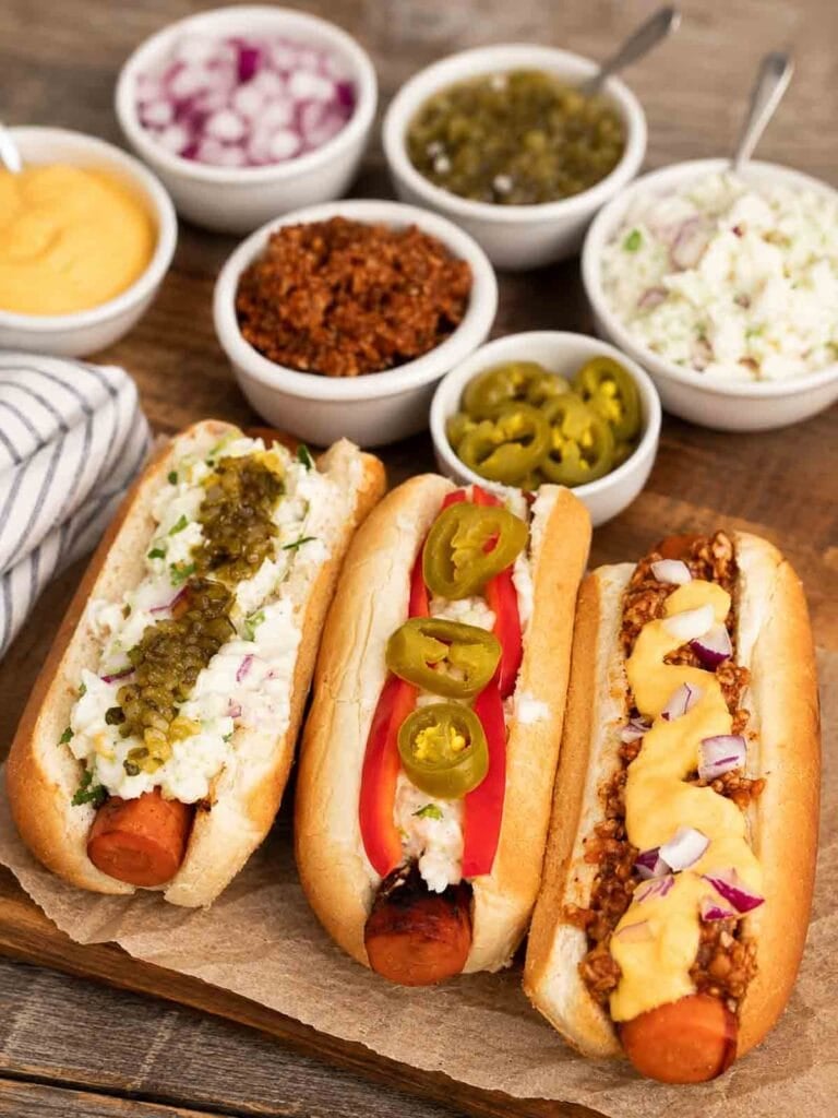 vegan hotdogs made from carrots with bowls of toppings sitting around them.