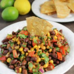 white bowl of black bean and corn salsa with a chip dipped